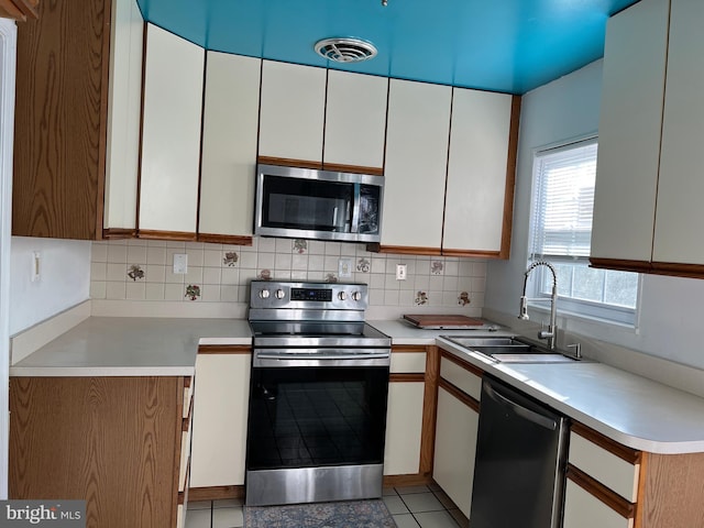 kitchen featuring tasteful backsplash, appliances with stainless steel finishes, light tile patterned floors, sink, and white cabinets