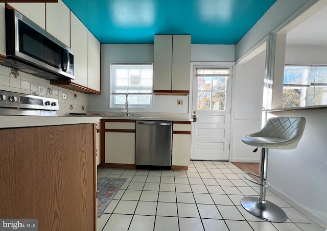 kitchen featuring white cabinets, appliances with stainless steel finishes, decorative backsplash, and plenty of natural light