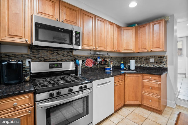 kitchen featuring sink, light tile patterned floors, dark stone counters, stainless steel appliances, and decorative backsplash