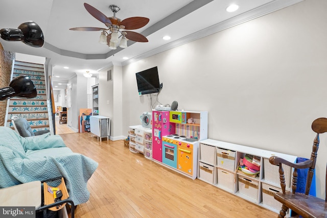 game room featuring a tray ceiling, hardwood / wood-style flooring, ornamental molding, and ceiling fan