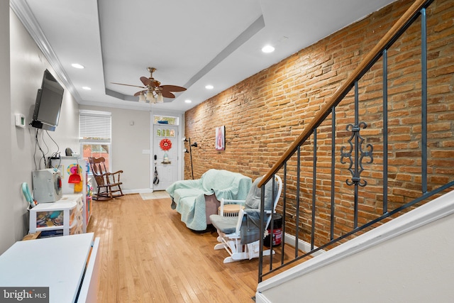 unfurnished living room with ceiling fan, brick wall, wood-type flooring, and a tray ceiling