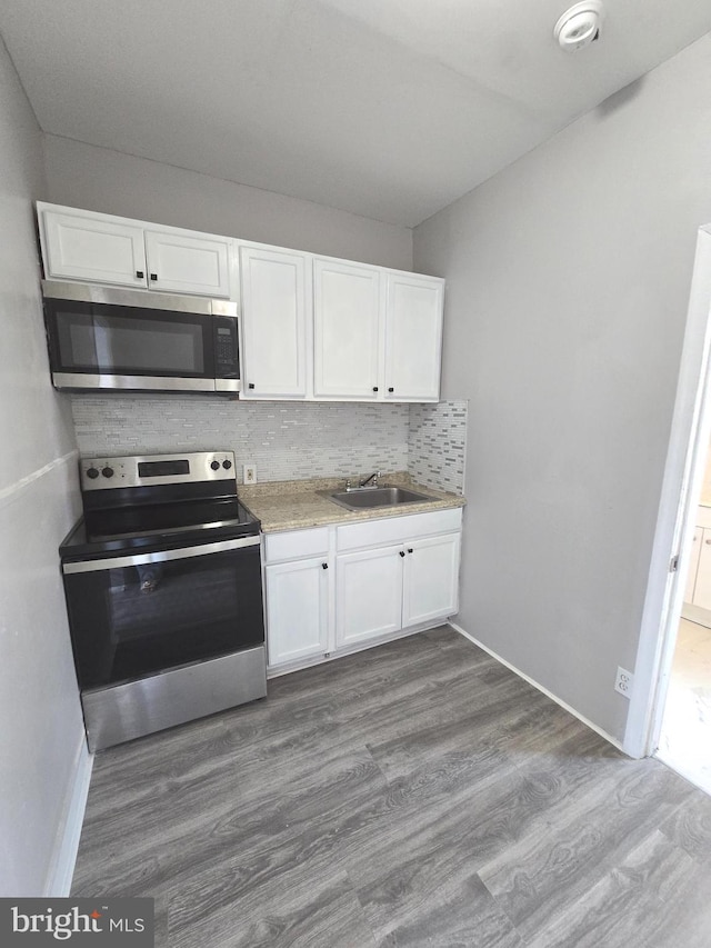 kitchen featuring stainless steel appliances, sink, tasteful backsplash, white cabinetry, and light wood-type flooring