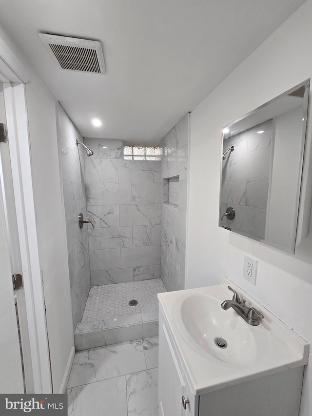 bathroom featuring marble finish floor, vanity, tiled shower, and visible vents