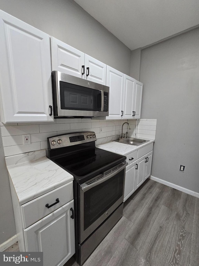 kitchen with dark wood finished floors, a sink, white cabinetry, decorative backsplash, and stainless steel appliances