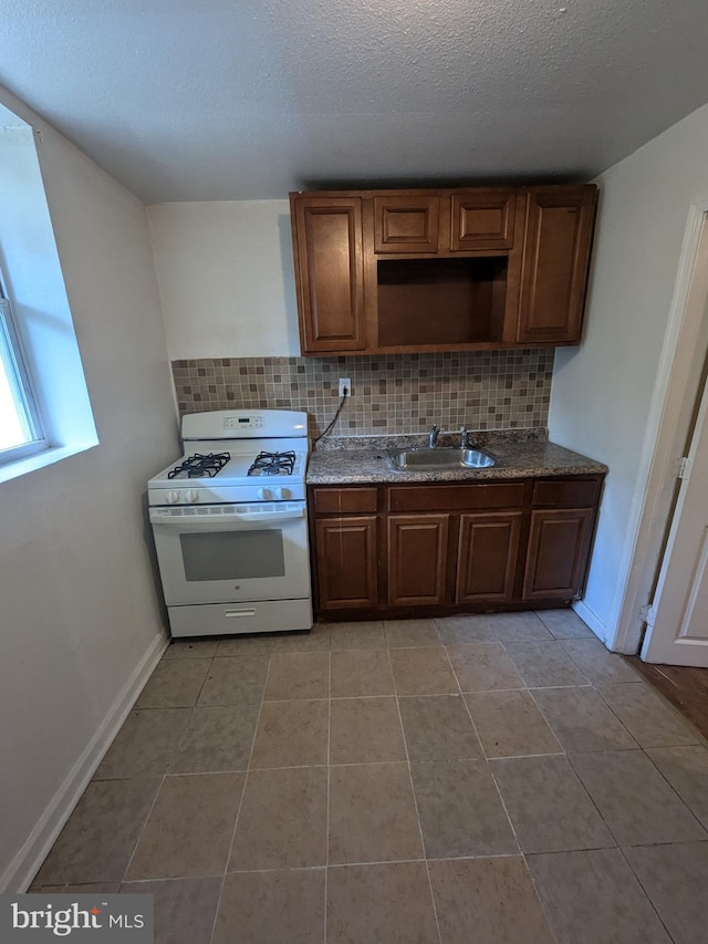 kitchen featuring white range with gas stovetop, backsplash, sink, and light tile patterned floors