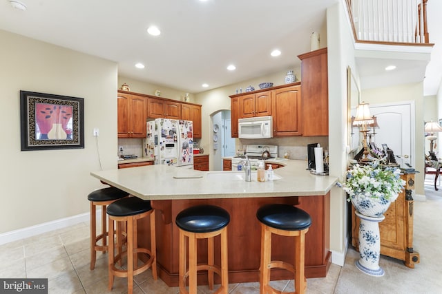 kitchen featuring kitchen peninsula, light tile patterned floors, a kitchen breakfast bar, backsplash, and white appliances