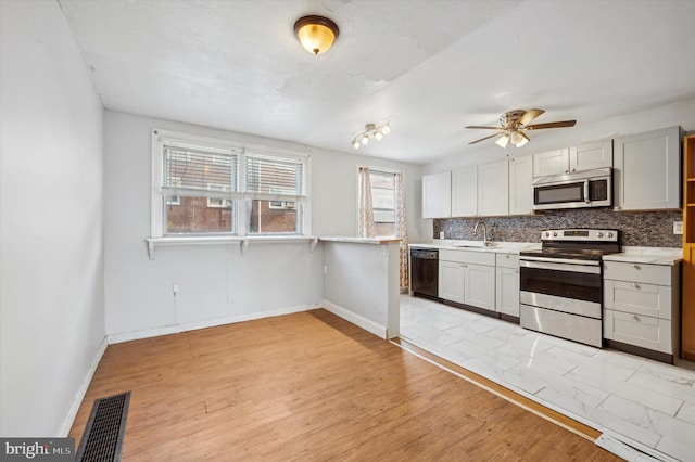 kitchen featuring backsplash, appliances with stainless steel finishes, sink, light hardwood / wood-style floors, and ceiling fan