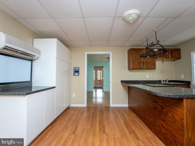 kitchen with kitchen peninsula, a drop ceiling, a wall mounted air conditioner, and light hardwood / wood-style floors