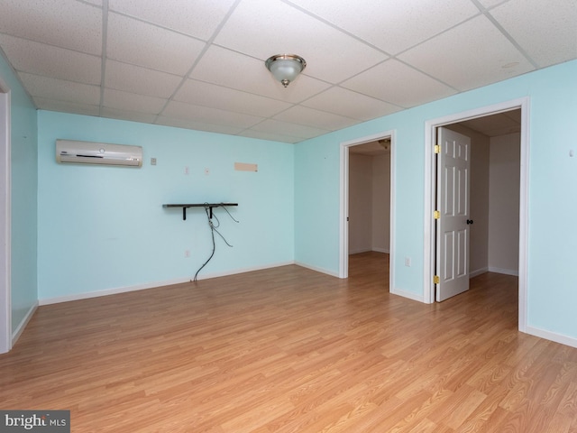 basement featuring a wall mounted AC, light wood-type flooring, and a drop ceiling