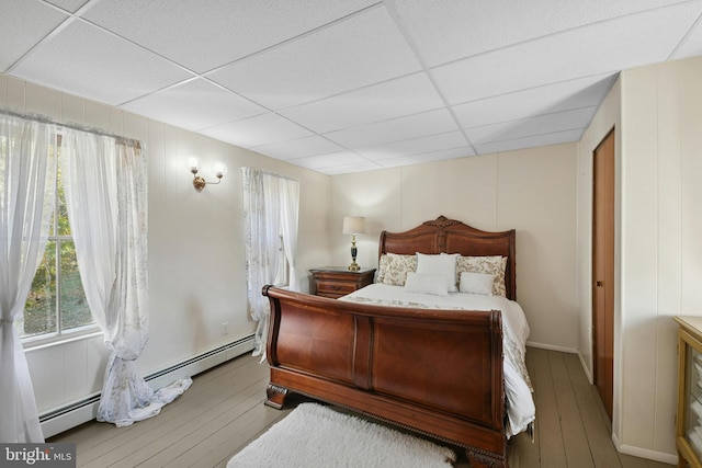 bedroom featuring baseboard heating, multiple windows, a drop ceiling, and wood-type flooring