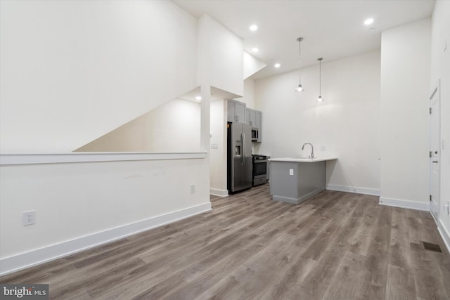 kitchen featuring appliances with stainless steel finishes, high vaulted ceiling, hanging light fixtures, hardwood / wood-style floors, and kitchen peninsula