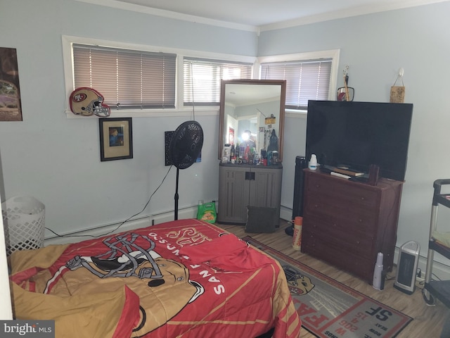 bedroom with hardwood / wood-style floors, a baseboard radiator, and crown molding