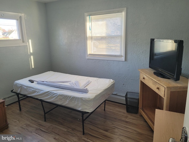 bedroom with a baseboard heating unit, dark wood-type flooring, and multiple windows