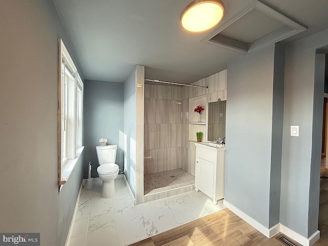 bathroom featuring toilet, vanity, wood-type flooring, and a tile shower