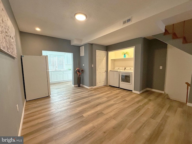 unfurnished living room with washing machine and dryer, a textured ceiling, and light wood-type flooring