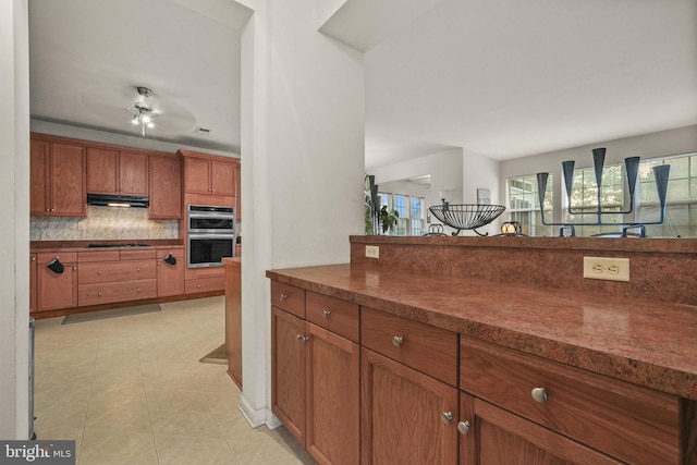 kitchen featuring tasteful backsplash, stainless steel double oven, light tile patterned flooring, black electric stovetop, and ceiling fan