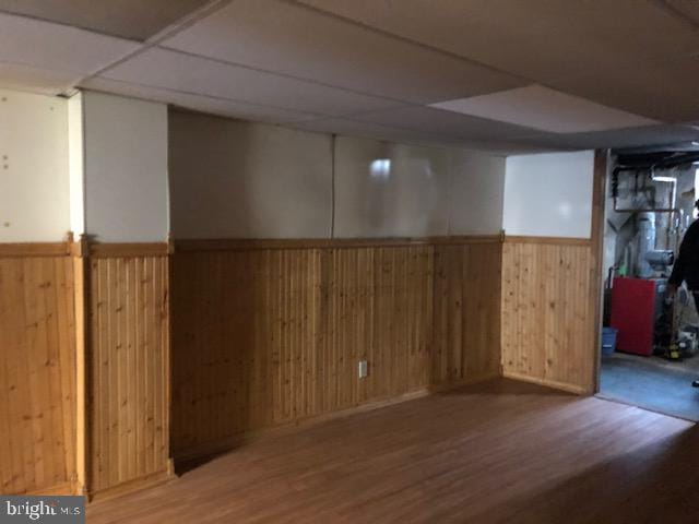 basement featuring hardwood / wood-style flooring, a paneled ceiling, and wooden walls