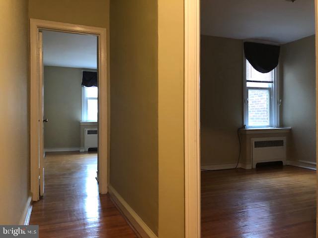 corridor with dark hardwood / wood-style flooring and radiator heating unit