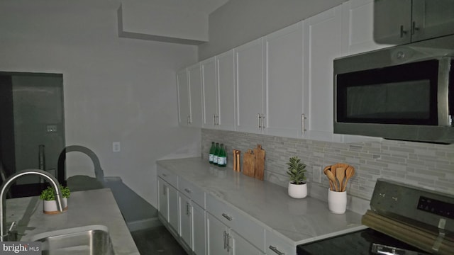 kitchen featuring white cabinets, stove, decorative backsplash, and sink