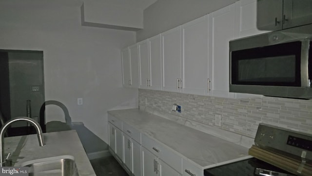 kitchen with decorative backsplash, white cabinetry, range, and sink