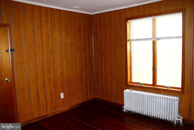 unfurnished room with dark wood-type flooring, wood walls, radiator heating unit, and ornamental molding