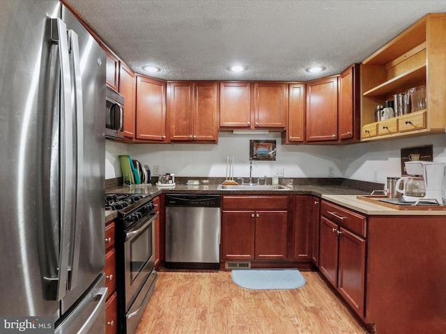 kitchen with a textured ceiling, stainless steel appliances, light hardwood / wood-style flooring, and sink