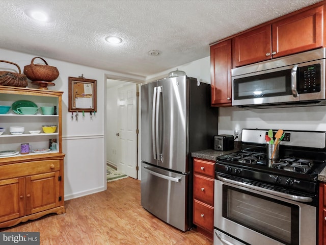 kitchen with stainless steel appliances, a textured ceiling, and light wood-type flooring