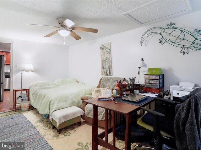 bedroom with a textured ceiling, stainless steel refrigerator, and ceiling fan