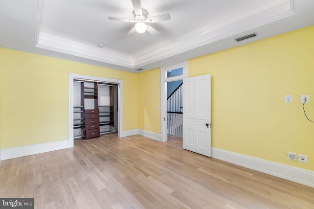 unfurnished bedroom with light hardwood / wood-style floors, ceiling fan, and a tray ceiling