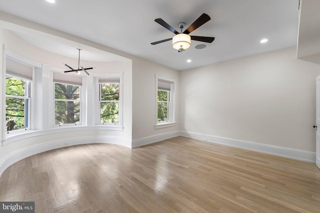 unfurnished room with light wood-type flooring and ceiling fan with notable chandelier