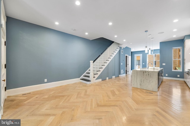 kitchen with sink, light stone counters, decorative light fixtures, light parquet flooring, and a spacious island