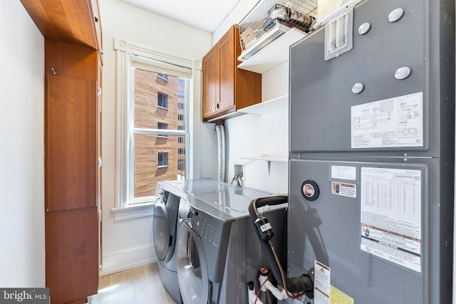 laundry room with heating unit, light wood-type flooring, cabinets, and washing machine and dryer