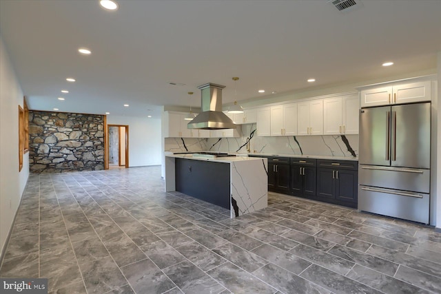 kitchen featuring backsplash, hanging light fixtures, stainless steel fridge, island range hood, and white cabinetry