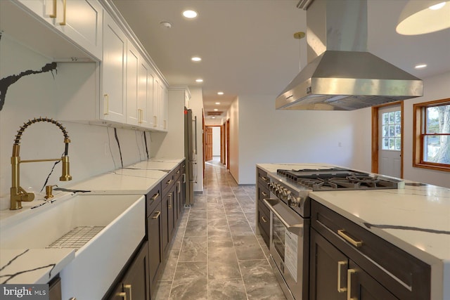 kitchen with pendant lighting, white cabinets, high end stainless steel range oven, light stone countertops, and range hood