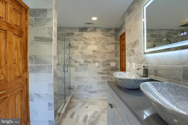 bathroom with vanity, a shower with door, and tile walls