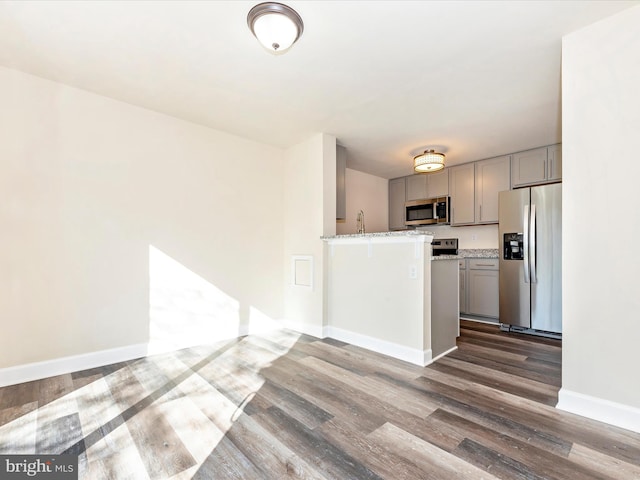 kitchen with stainless steel appliances, sink, light stone countertops, dark wood-type flooring, and gray cabinetry