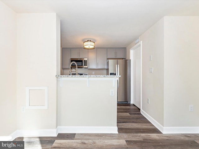 kitchen featuring stainless steel appliances, dark wood-type flooring, light stone counters, a breakfast bar area, and gray cabinets