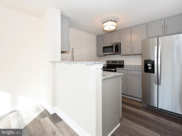 kitchen with gray cabinets, stainless steel appliances, light stone counters, and dark hardwood / wood-style flooring