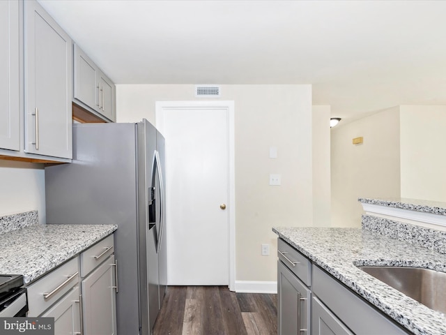 kitchen featuring stainless steel fridge, gray cabinets, dark hardwood / wood-style flooring, and light stone countertops