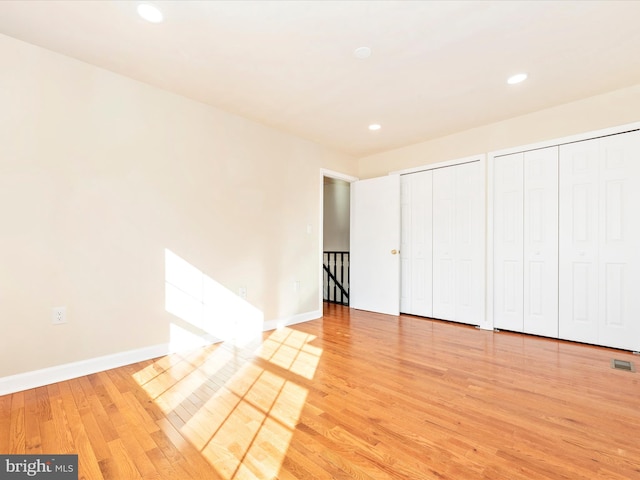 unfurnished bedroom featuring multiple closets and light hardwood / wood-style floors