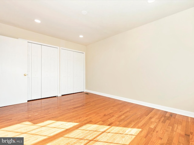 unfurnished bedroom featuring wood-type flooring and two closets