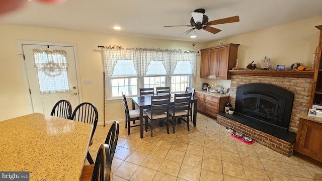 tiled dining space with ceiling fan and a brick fireplace