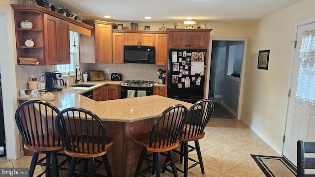 kitchen with sink, tasteful backsplash, a kitchen bar, light tile patterned floors, and black appliances