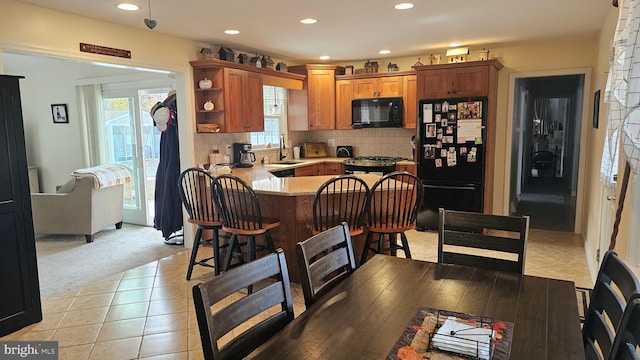 kitchen with kitchen peninsula, decorative backsplash, a kitchen bar, light colored carpet, and black appliances