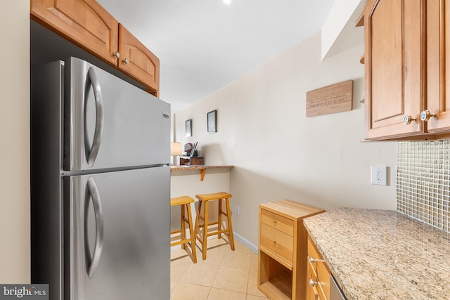 kitchen featuring light tile patterned flooring, stainless steel fridge, light stone counters, and tasteful backsplash