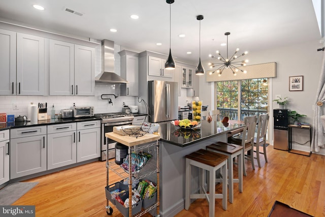 kitchen featuring a kitchen bar, light wood-type flooring, stainless steel appliances, and wall chimney range hood