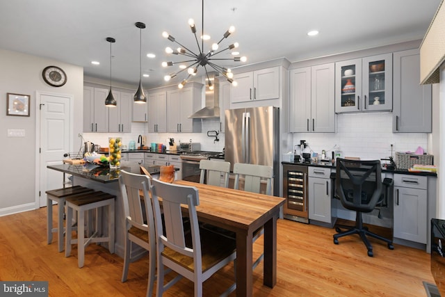 kitchen with appliances with stainless steel finishes, beverage cooler, wall chimney range hood, gray cabinetry, and pendant lighting