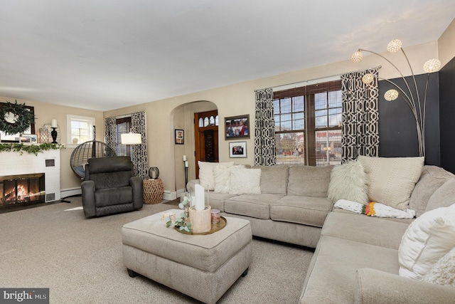 carpeted living room with baseboard heating, arched walkways, a fireplace with flush hearth, and baseboards