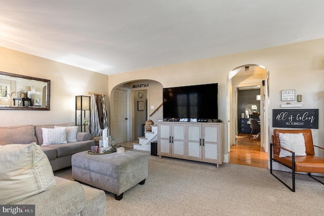 living area featuring light colored carpet, stairs, and arched walkways