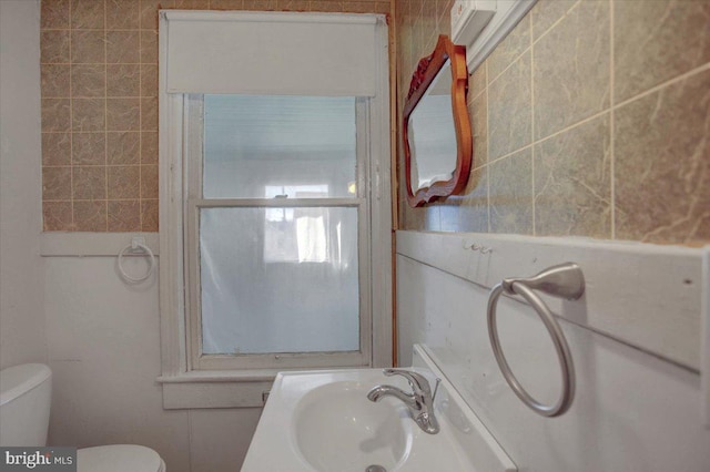 bathroom with toilet, tile walls, and sink